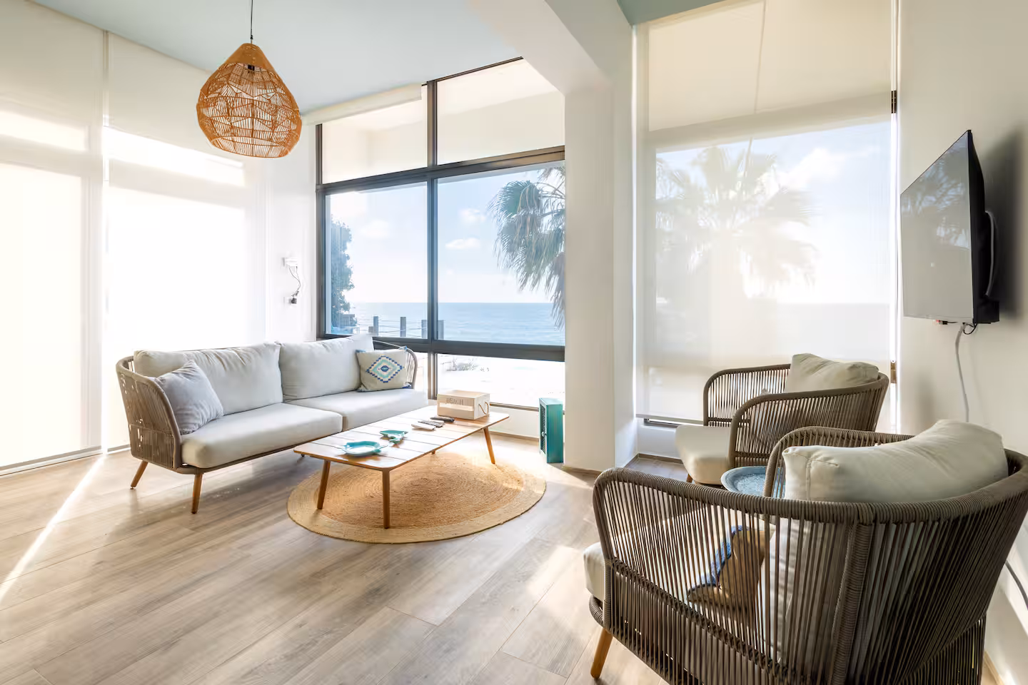 Bright chalet living room with rope armchairs, jute rug and sea view through corner windows