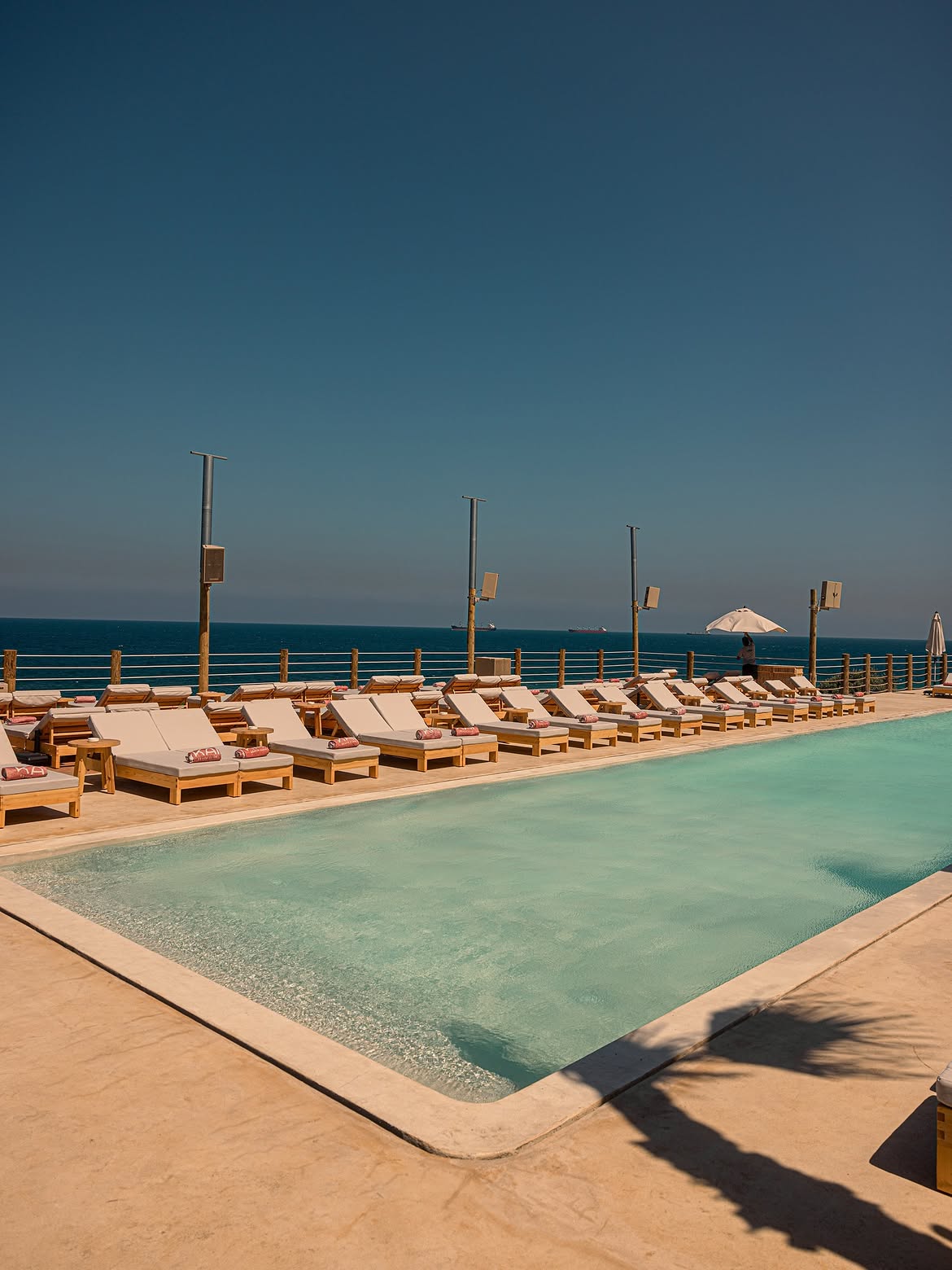 Empty loungers along the turquoise pool under a deep blue sky