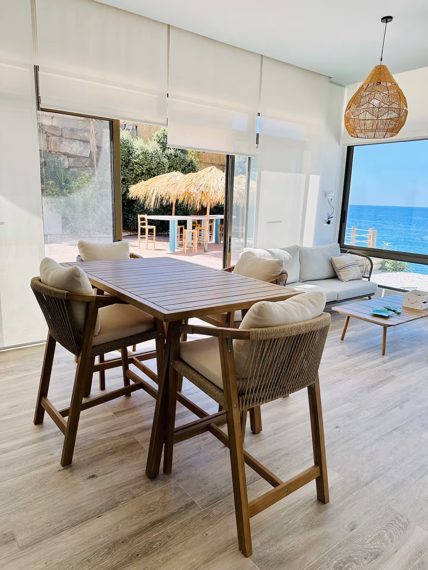 Open chalet dining area with a timber table, rope chairs and sliding doors onto the sea deck