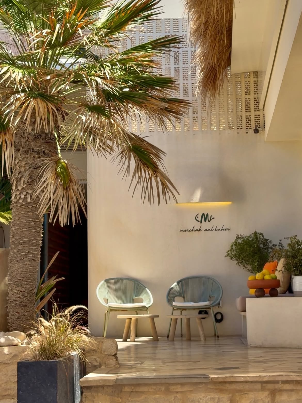 Merchak Aal Baher entrance with cream walls, woven chairs and a palm tree