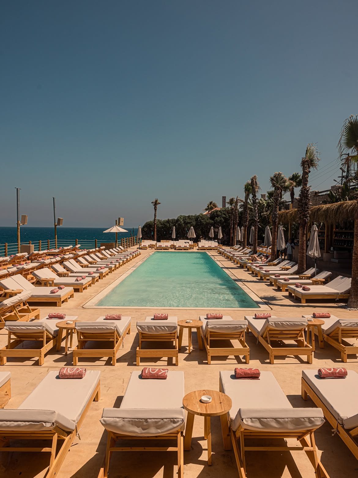 The Kai pool seen head-on, loungers in rows on the limestone deck with the sea behind
