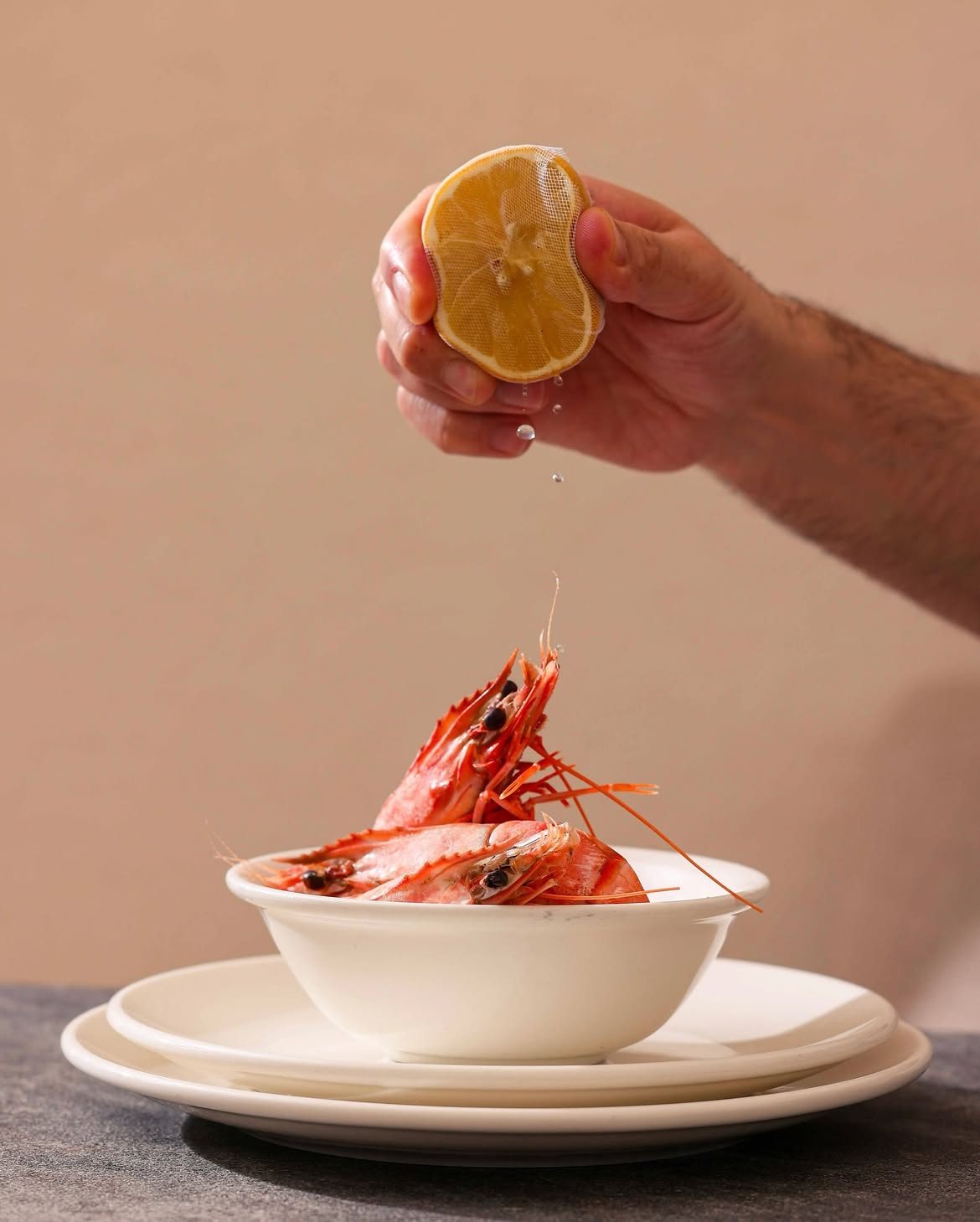 Hand squeezing lemon over a bowl of prawns