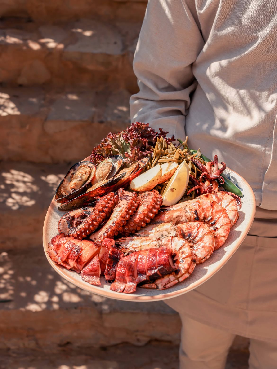 Waiter carrying a large platter of grilled prawns, octopus and mussels