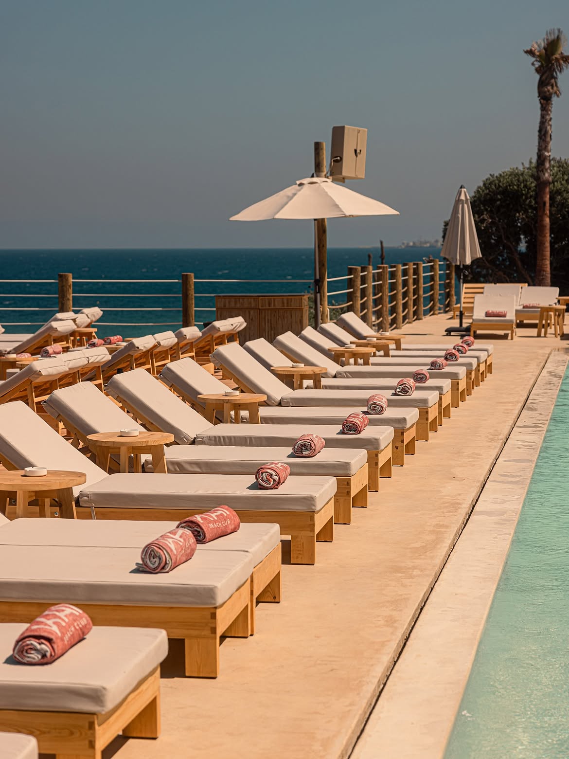 Row of timber loungers with rolled Kai towels along the edge of the pool